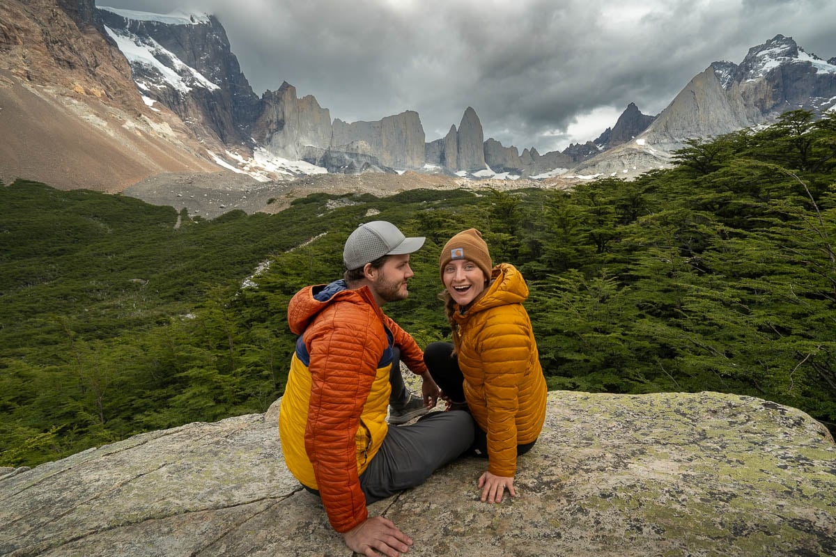 Couple sitting on a rocky outcropping with jagged mountains in the background along the W Trek in Torres del Paine National Park in Patagonia