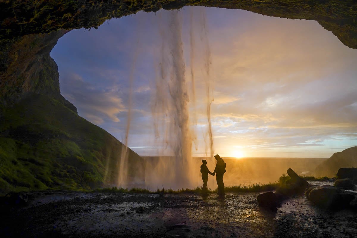 Couple holding hands with Seljalandsfoss in the background at sunset in Iceland