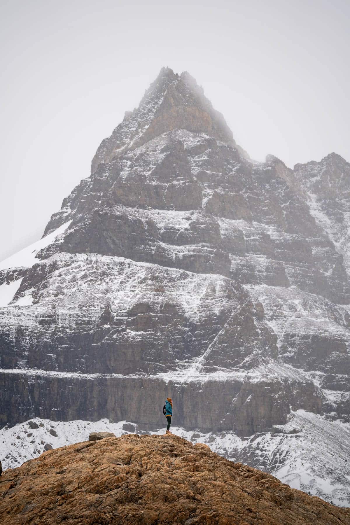 Woman standing on a rocky outcropping in front of a large snowy mountain along the Laguna de los Tres Trail in El Chalten, Argentina