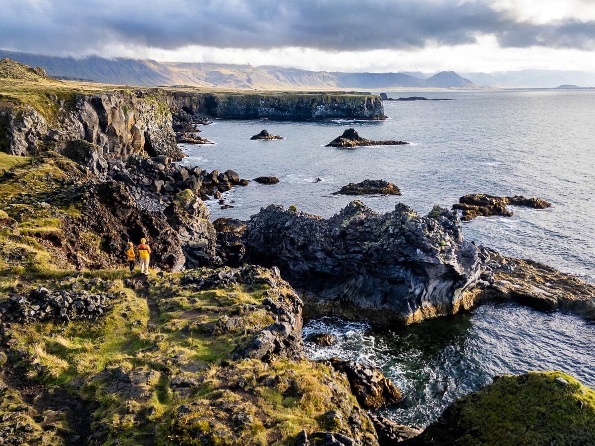 Couple standing on a rugged cliffside on the path from Arnastapi to Hellnar on the Snæfellsnes Peninsula in Iceland