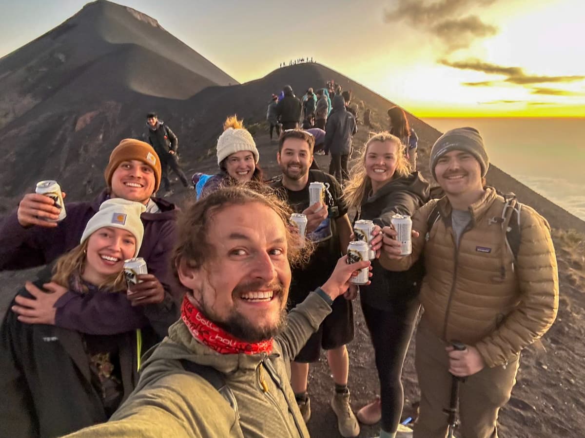 Group of hikers standing on Fuego Volcano with a beer at sunset along the Acatenango Hike in Guatemala