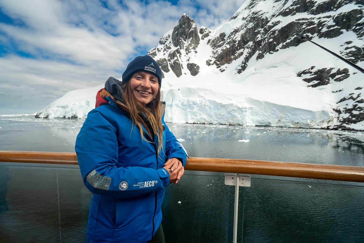 Woman smiling on the top deck with snowy mountains in the background in the Lemaire Channel on an Antarctica cruise