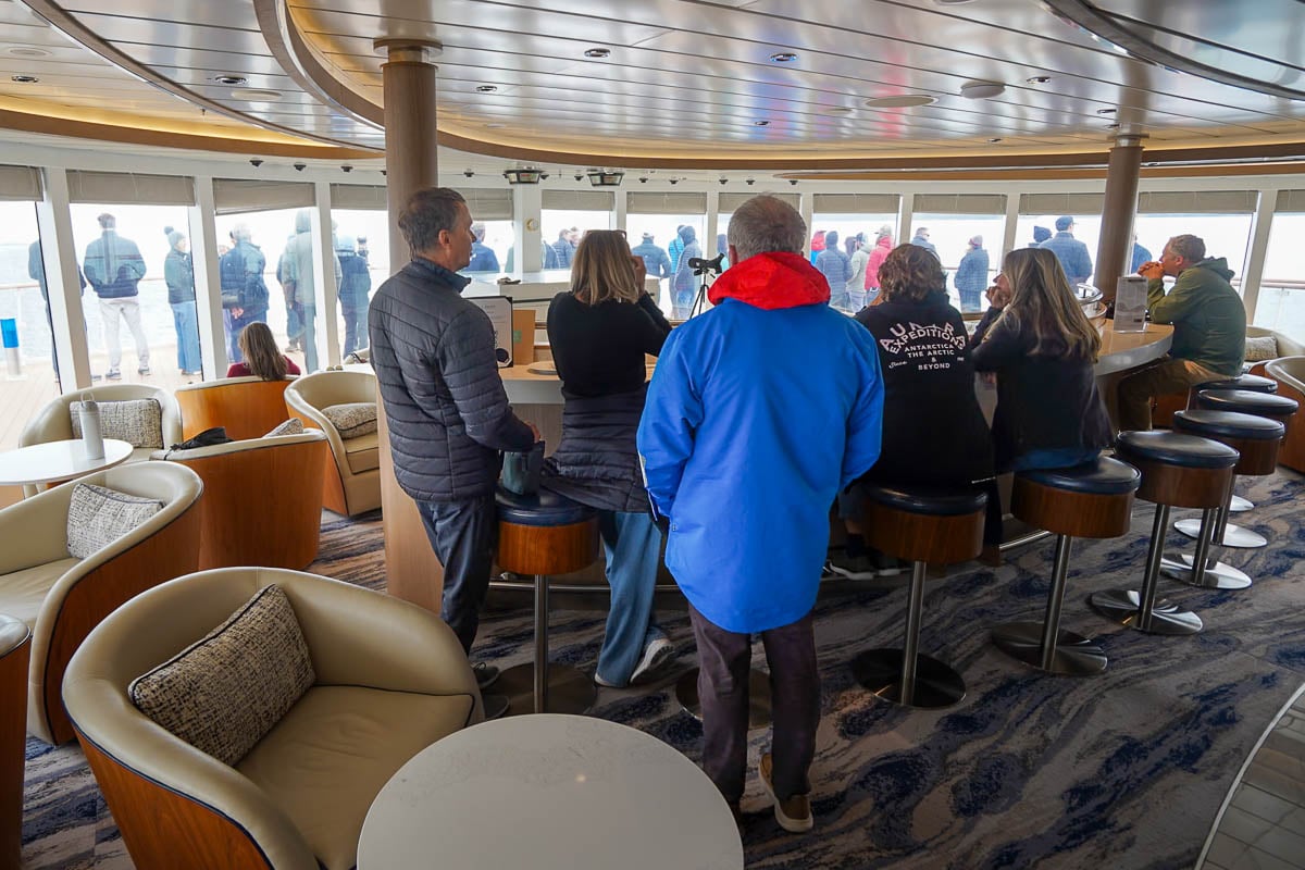 Passengers sitting in the observation lounge on the Greg Mortimer ship on an Antarctica cruise