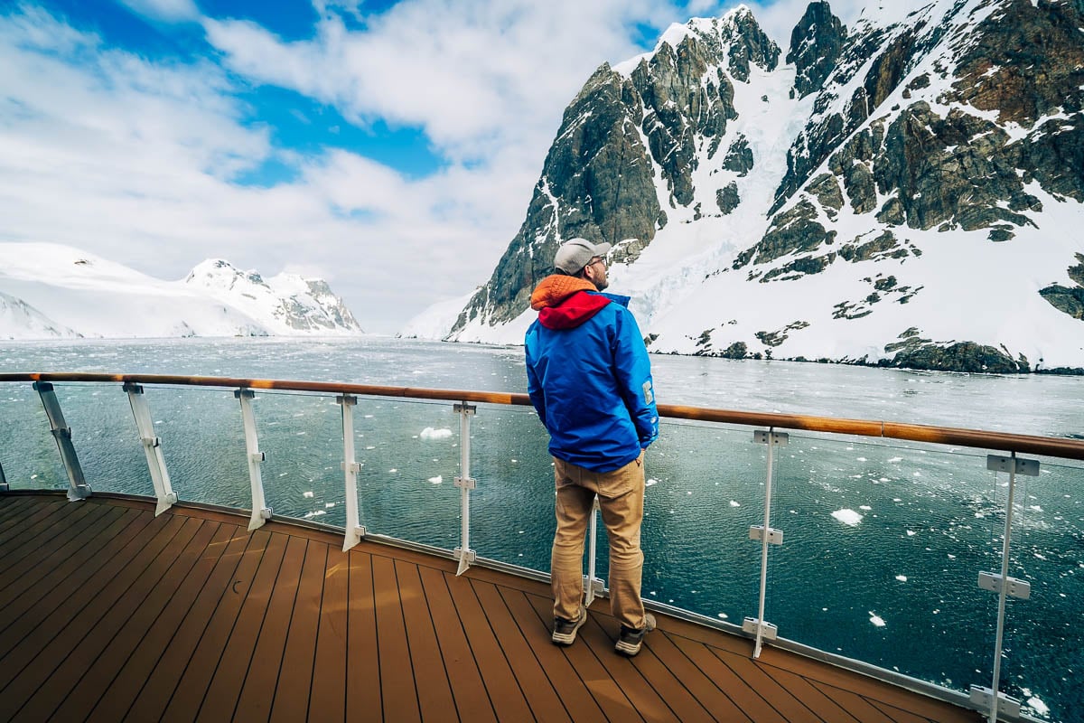 Man standing on a top deck looking at snowy mountains in the Lemaire Channel on an Antarctica cruise