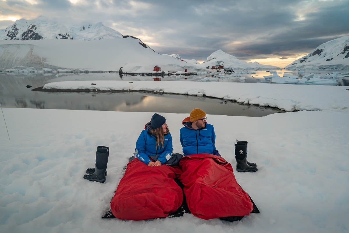 Couple sitting in bivy bags while on a camping trip in Paradise Bay on an Antarctica cruise