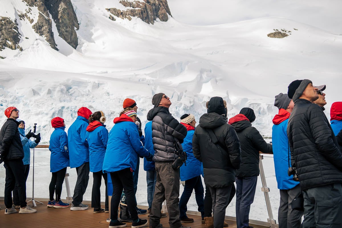 Passengers on the Aurora Expeditions Greg Mortimer ship sailing through the Lemaire Channel with glaciers in the background in Antarctica