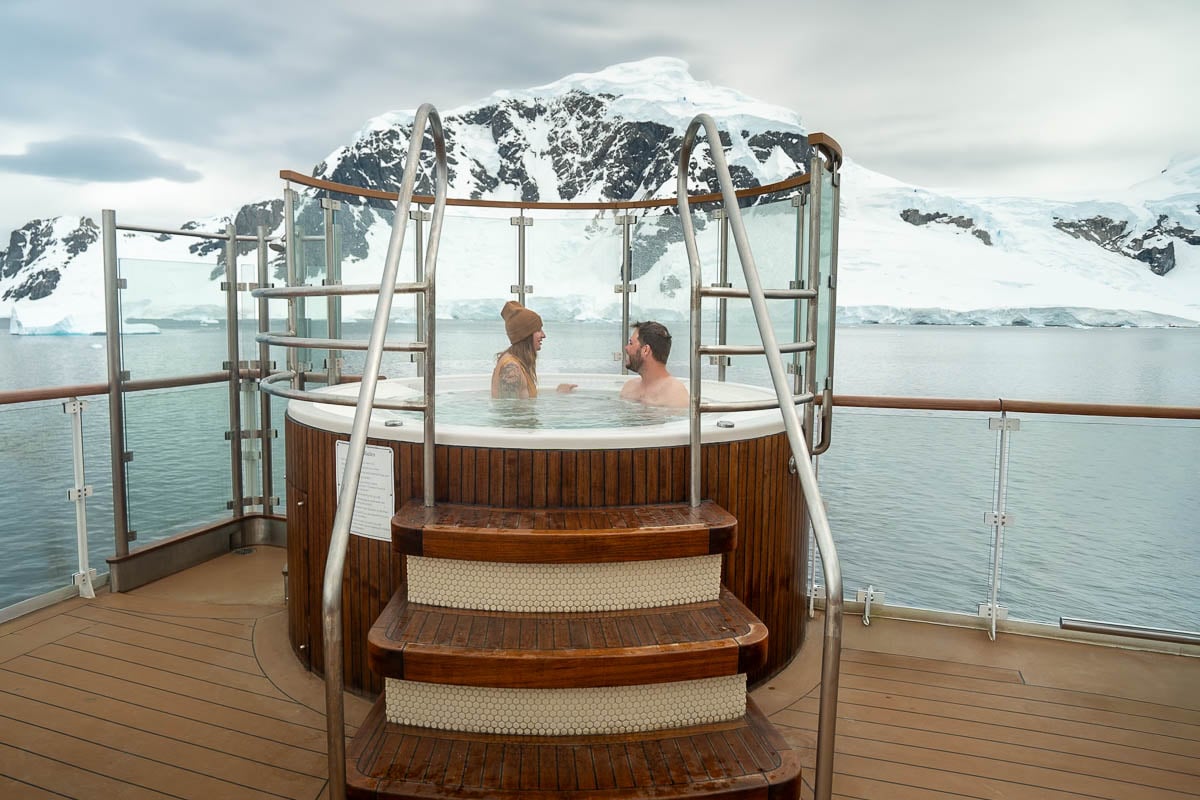 Couple sitting in a hot tub on Aurora Expeditions Greg Mortimer with snow-capped mountains in the background in Antarctica