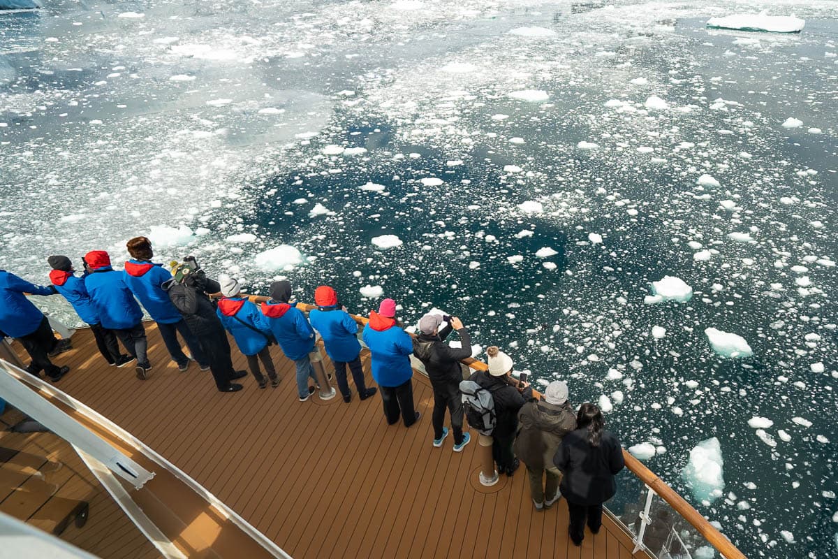 People standing on the deck of the Aurora Expeditions Greg Mortimer looking at ice in the water in the Lemaire Channel in Antarctica
