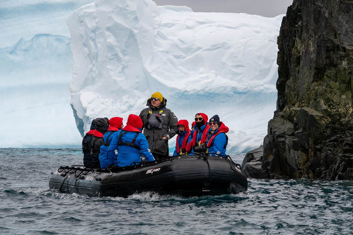 Expedition guide with passengers on Aurora Expeditions with rocky cliffs and icebergs in the background in Spert Island, Antarctica