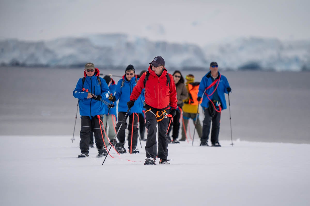 Guide and passengers snowshoeing on a mountain ridge at Damoy Point in Antarctica