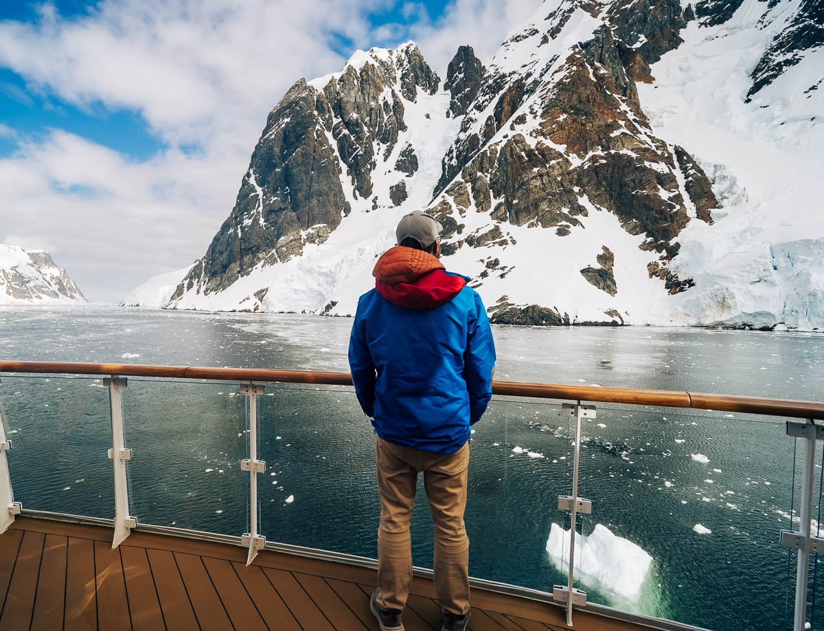 Man standing on the top deck of Aurora Expeditions Greg Mortimer ship, while looking at a snowy mountain in the Lemaire Channel of Antarctica