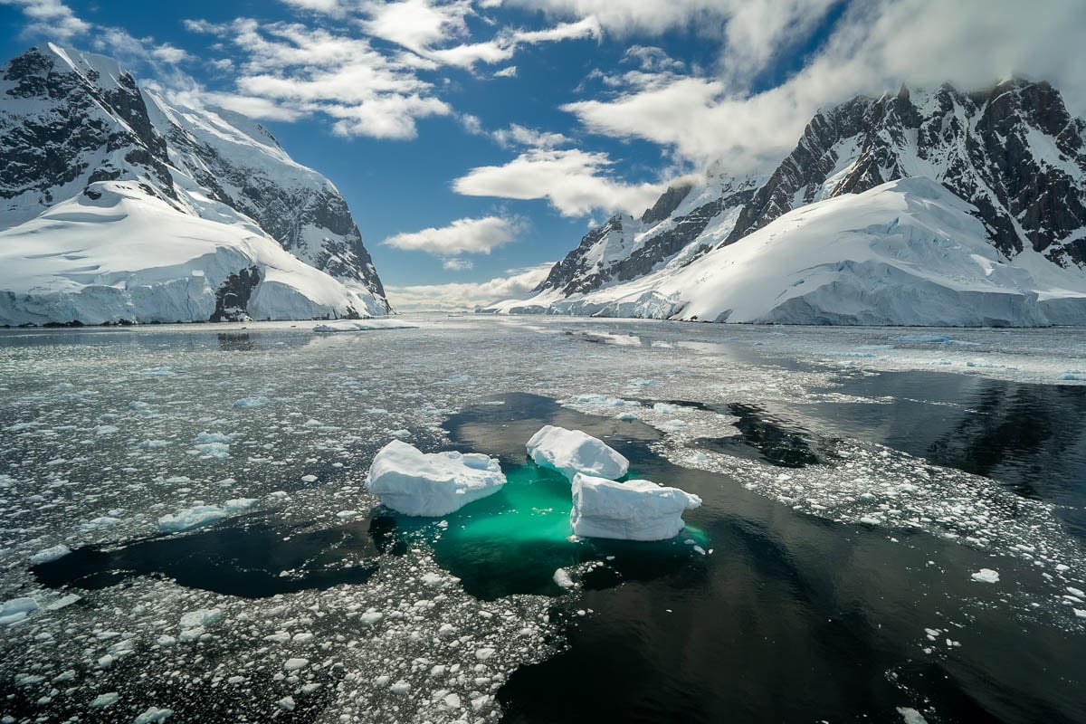 Icebergs surrounded by bits of ice with snowy mountains in the background in the Lemaire Channel in Antarctica