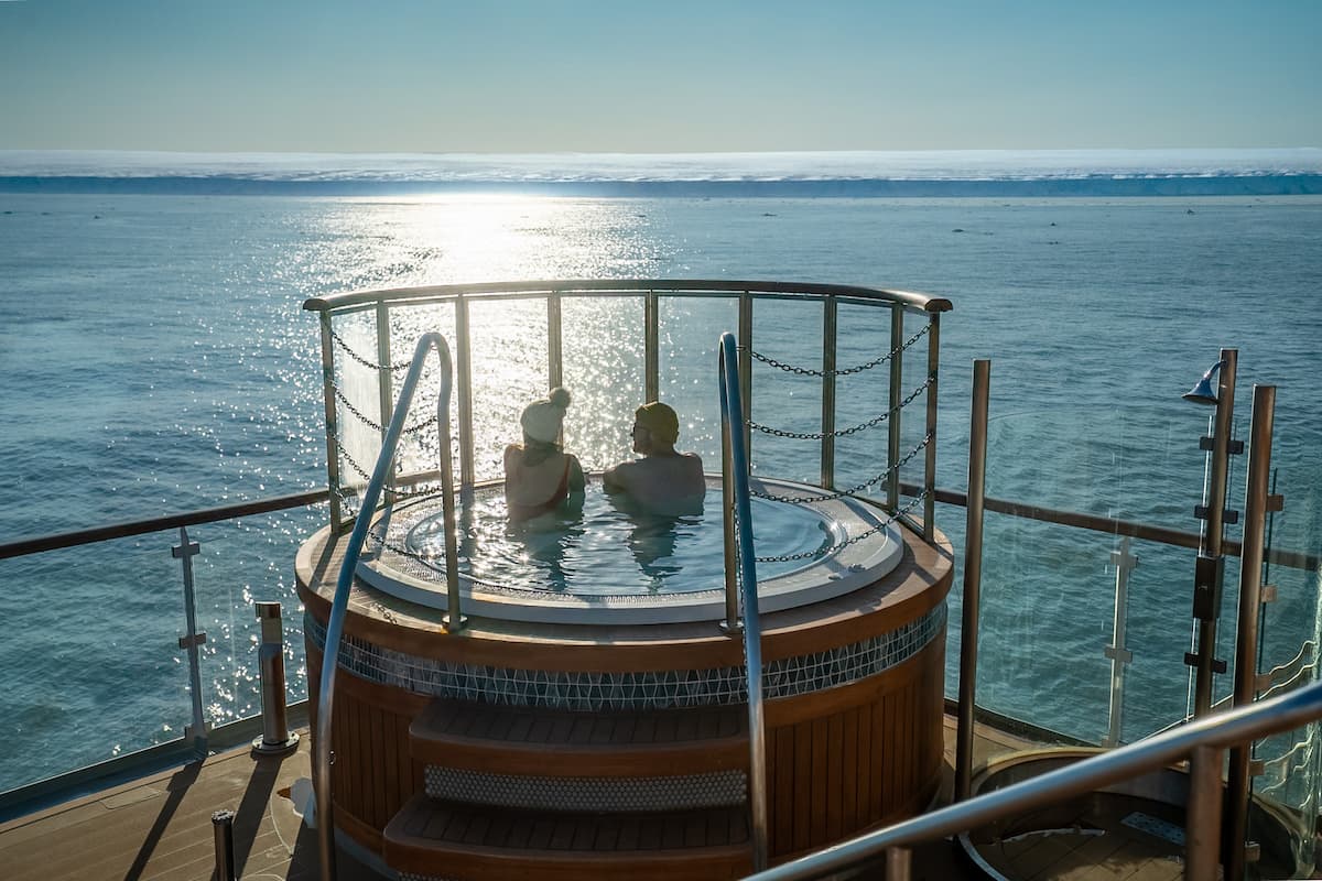 Couple sitting in a hot tub while looking at a wall of ice on Aurora Expeditions Sylvia Earle ship in Svalbard, Norway