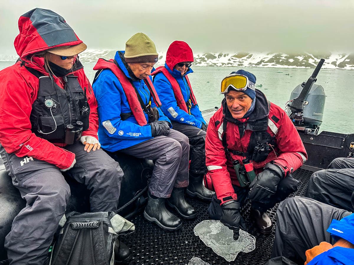Aurora Expeditions guide pointing at ice on the floor of a zodiac boat with foggy mountains in the background in Svalbard, Norway