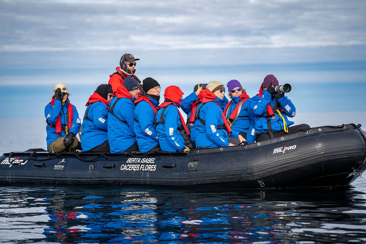 Aurora Expeditions guide standing on a Zodiac boat with guests taking photos in Svalbard, Norway