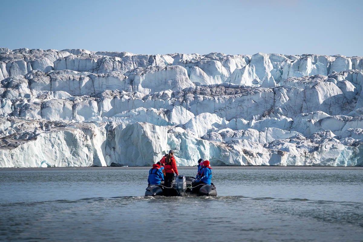 Aurora Expeditions guide steering a Zodiac cruise with a glacier in the background in Svalbard, Norway