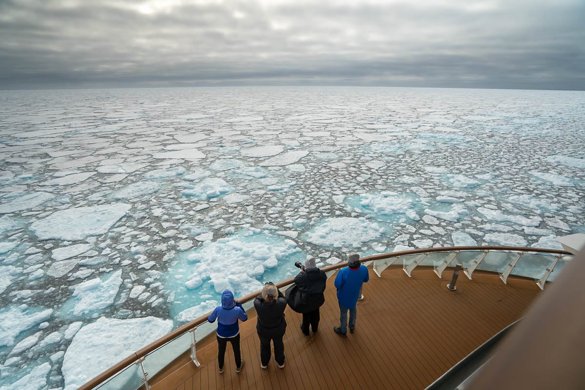 Passengers standing on an observation deck on the Aurora Expeditions' Sylvia Earle ship with pack ice stretching towards the horizon in Svalbard, Norway