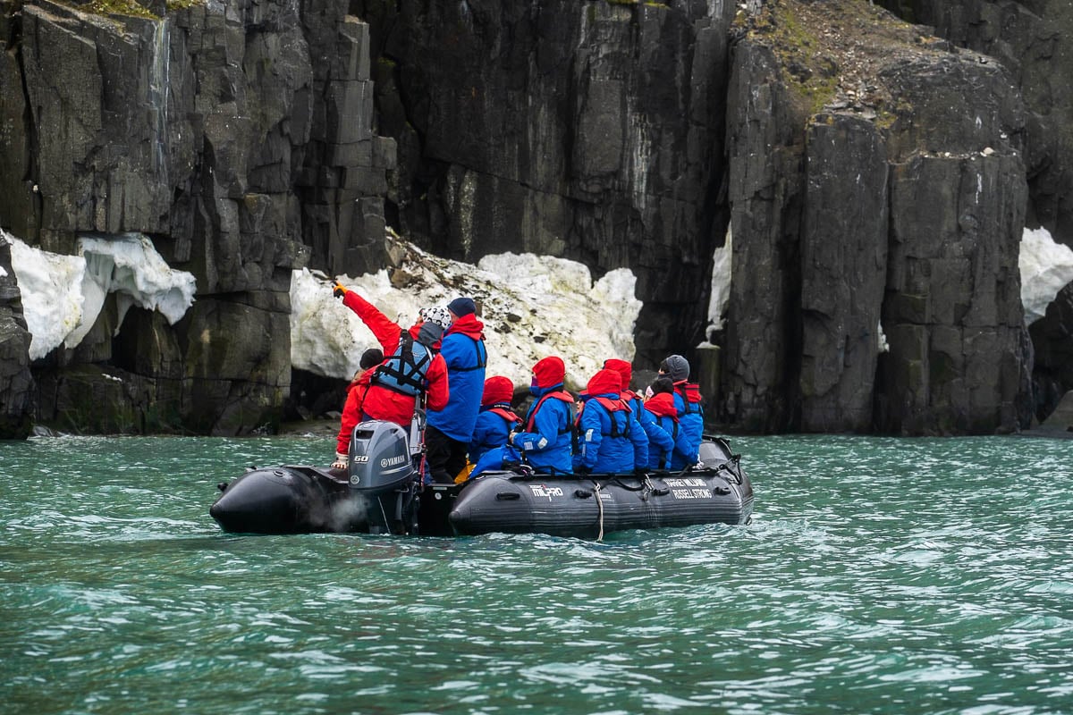 Expedition guide pointing out wildlife to a Zodiac boat with passengers on it with the volcanic cliffs of Alkefjellet in Svalbard, Norway