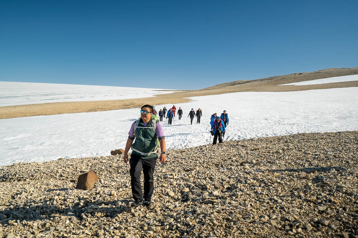 Man walking on a rocky slope with other hikers in the background in Svalbard, Norway