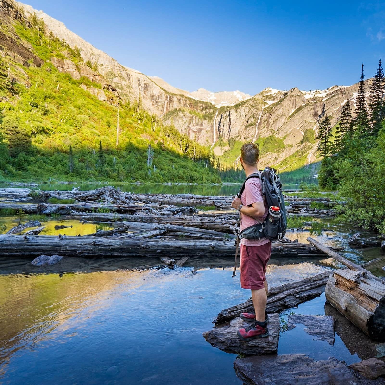 Man standing on a rock and looking at mountains at Avalanche Lake in Glacier National Park