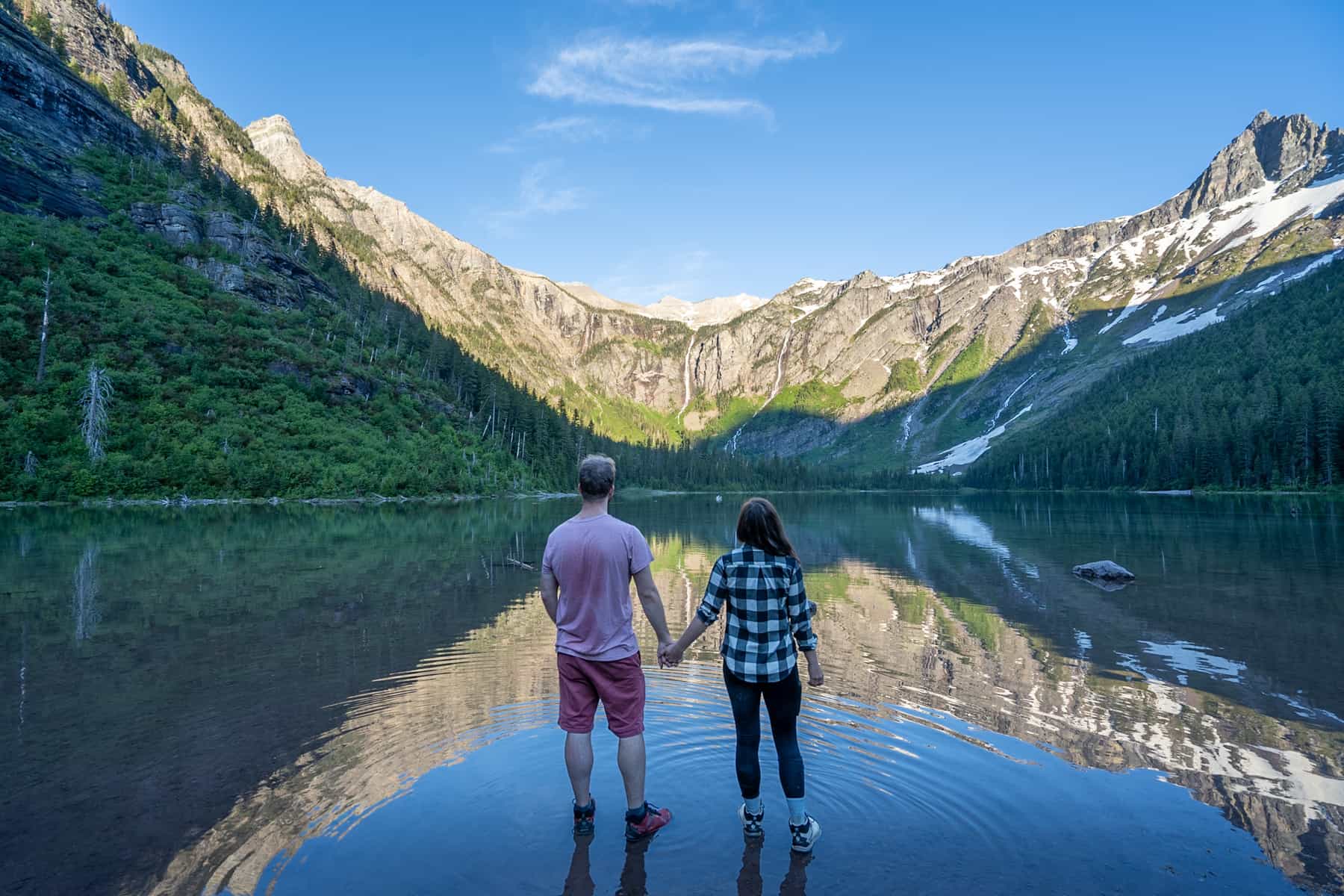 Couple holding hands in Avalanche Lake with the Rocky Mountains in the background along the Avalanche Lake Trail in Glacier National Park, Montana