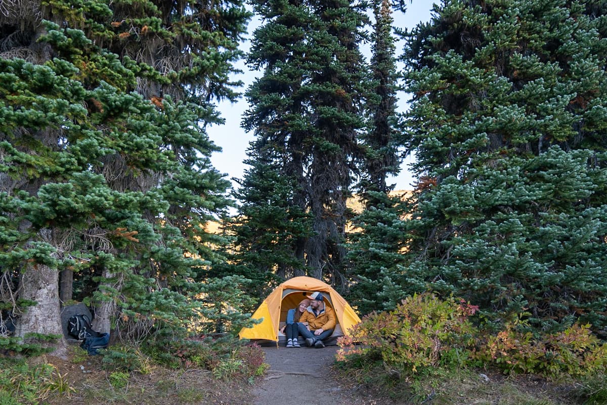 Couple sitting in a tent at Camp Summerland surrounded by pine trees along the Summerland Trail in Mount Rainier National Park