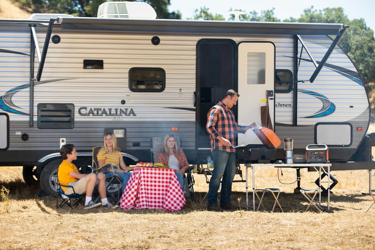 Family sitting outside a Coachmen Catalina trailer in a grass field