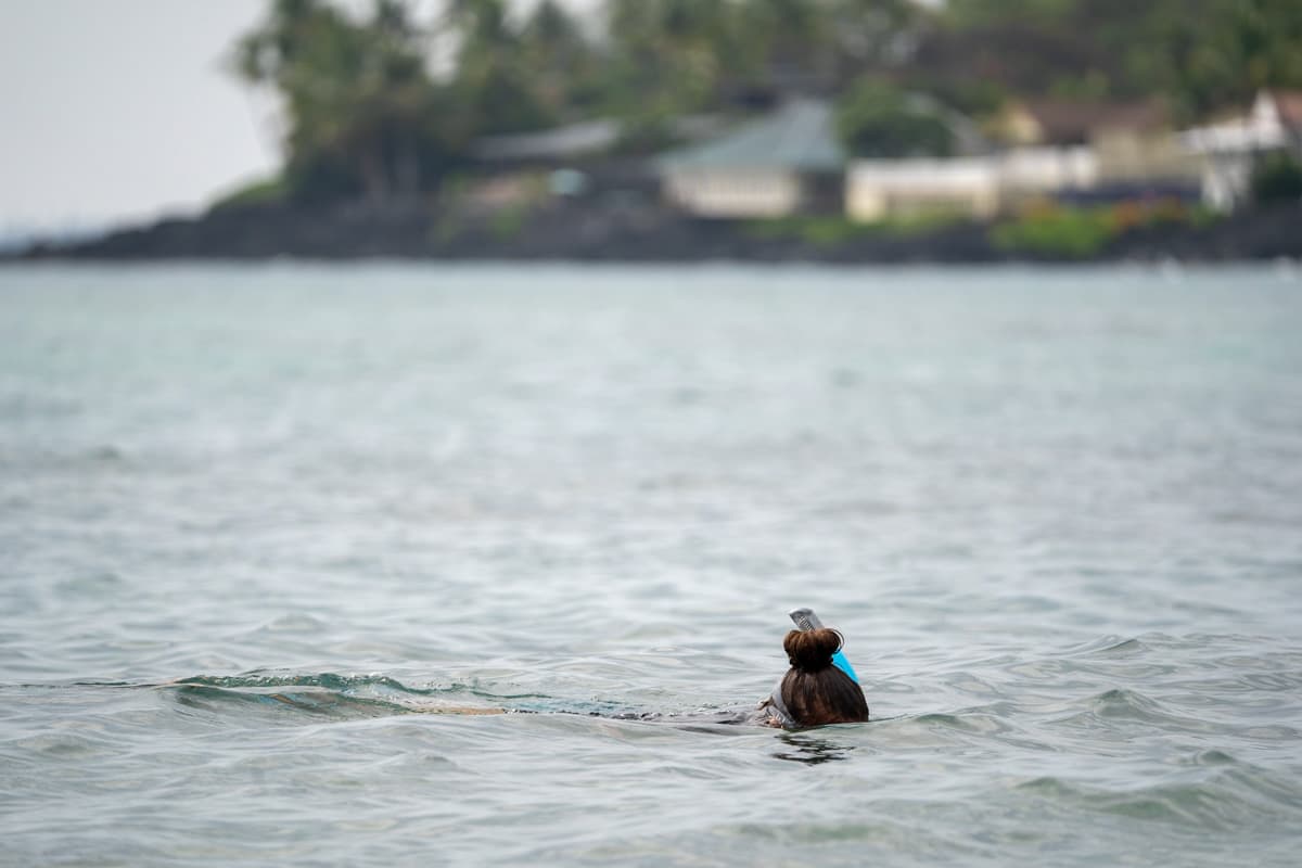 Woman snorkeling at Kahalu'u Beach with residential houses along the coastline in the background on the Big Island of Hawaii