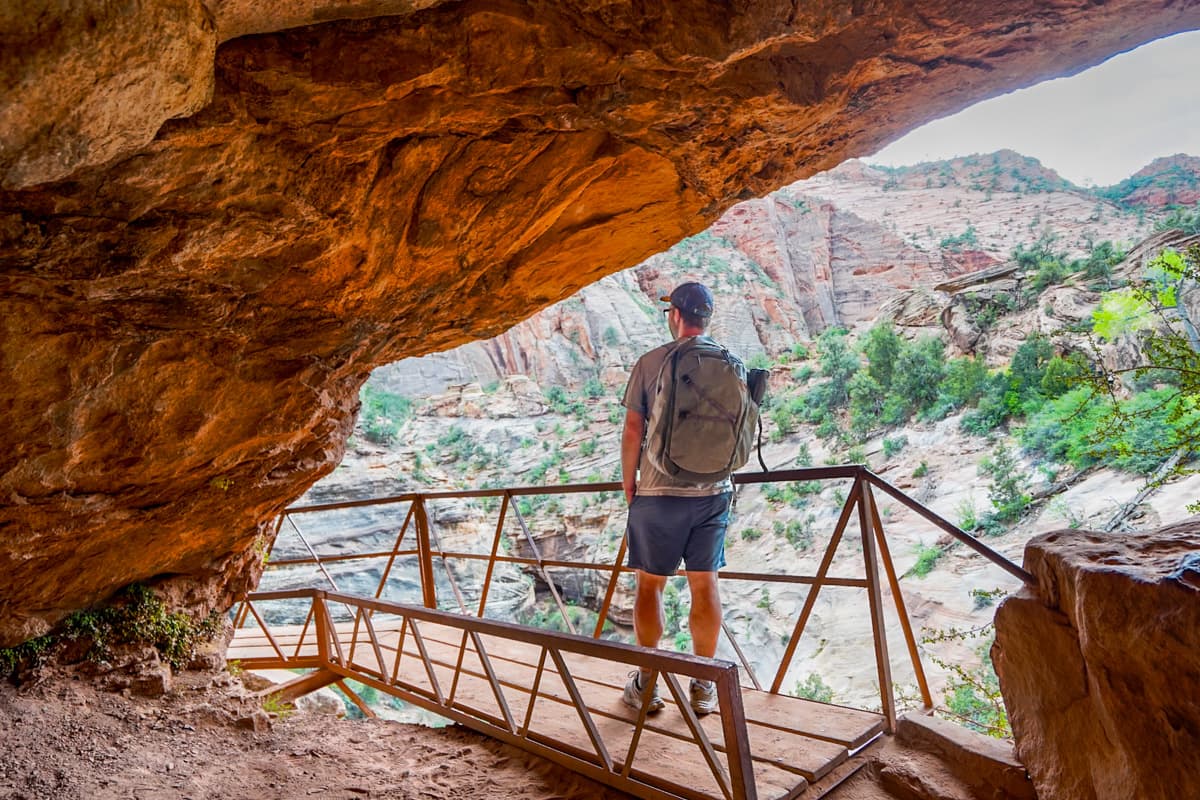 Man standing on a wooden boardwalk in a grotto along the Canyon Overlook Trail in Zion National Park