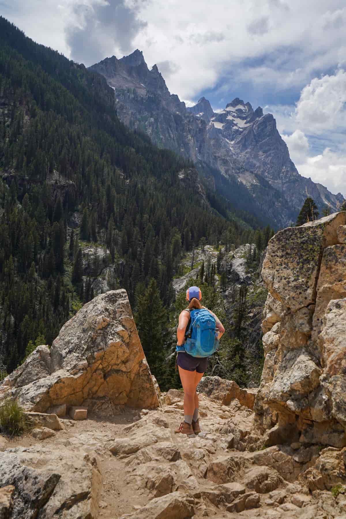 Woman standing along a rocky staircase with Teton Mountains in the background along the Cascade Canyon Trail in Grand Teton National Park in Wyoming