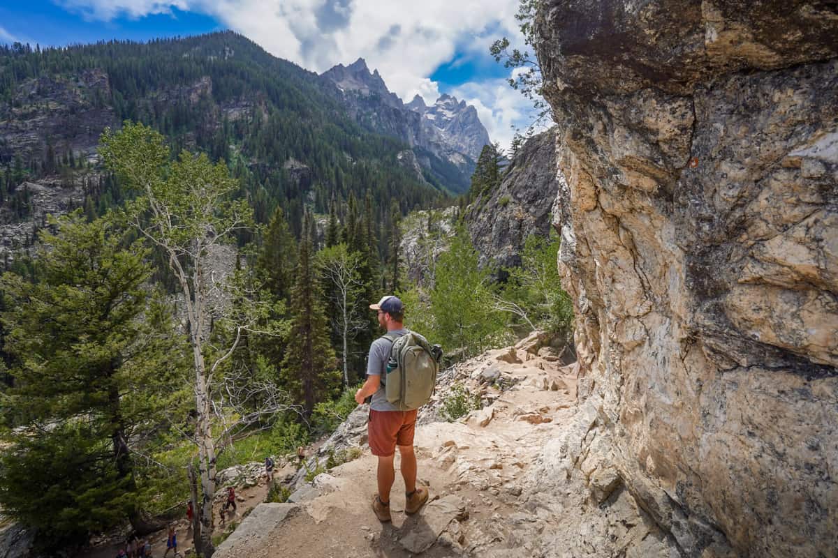 Man climbing up stone steps along a rocky cliffside with the Teton Mountain in the background along the Cascade Canyon Trail in Grand Teton National Park in Wyoming