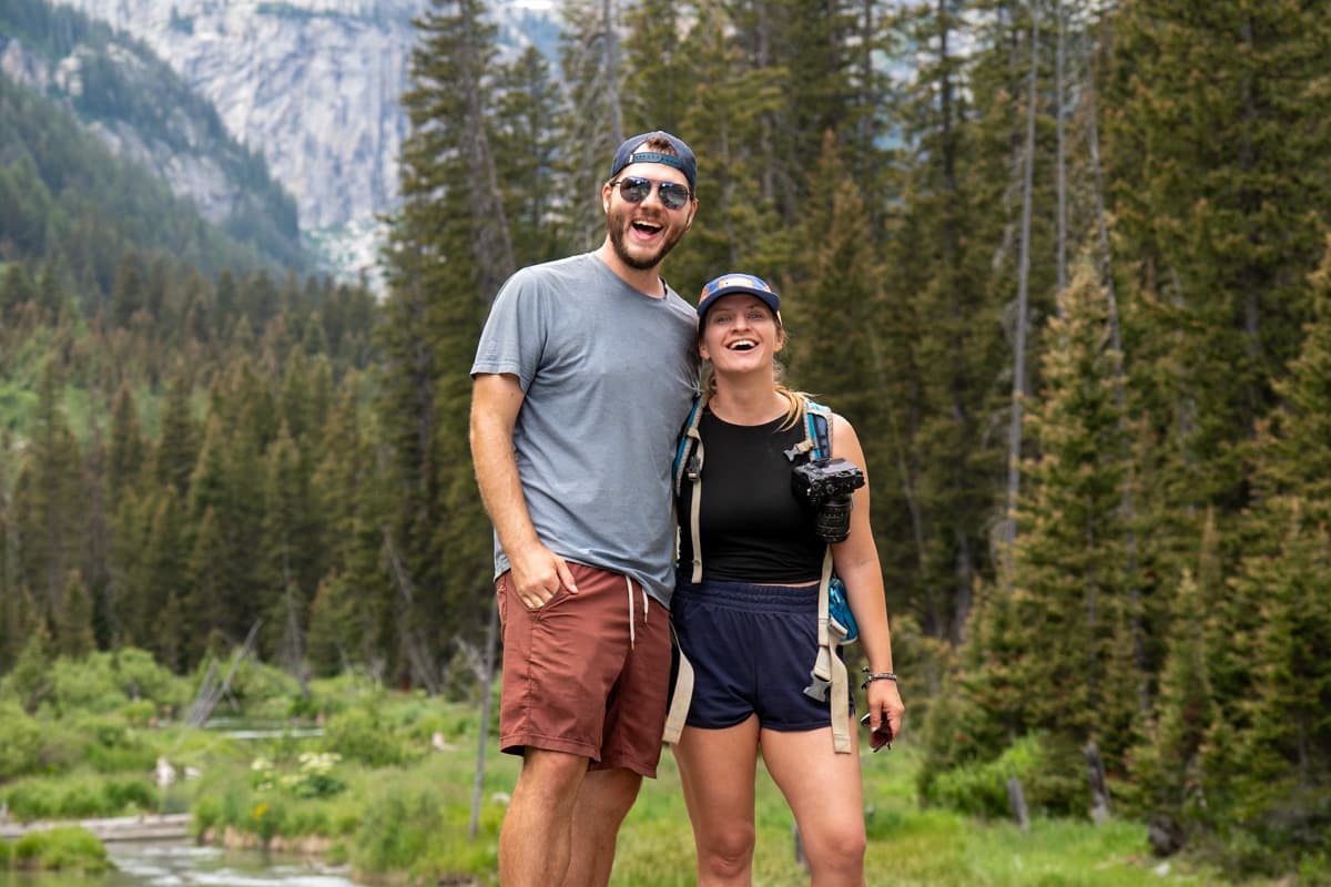 Smiling couple with pine trees and the Teton Mountains in the background along the Cascade Canyon Trail in Grand Teton National Park in Wyoming