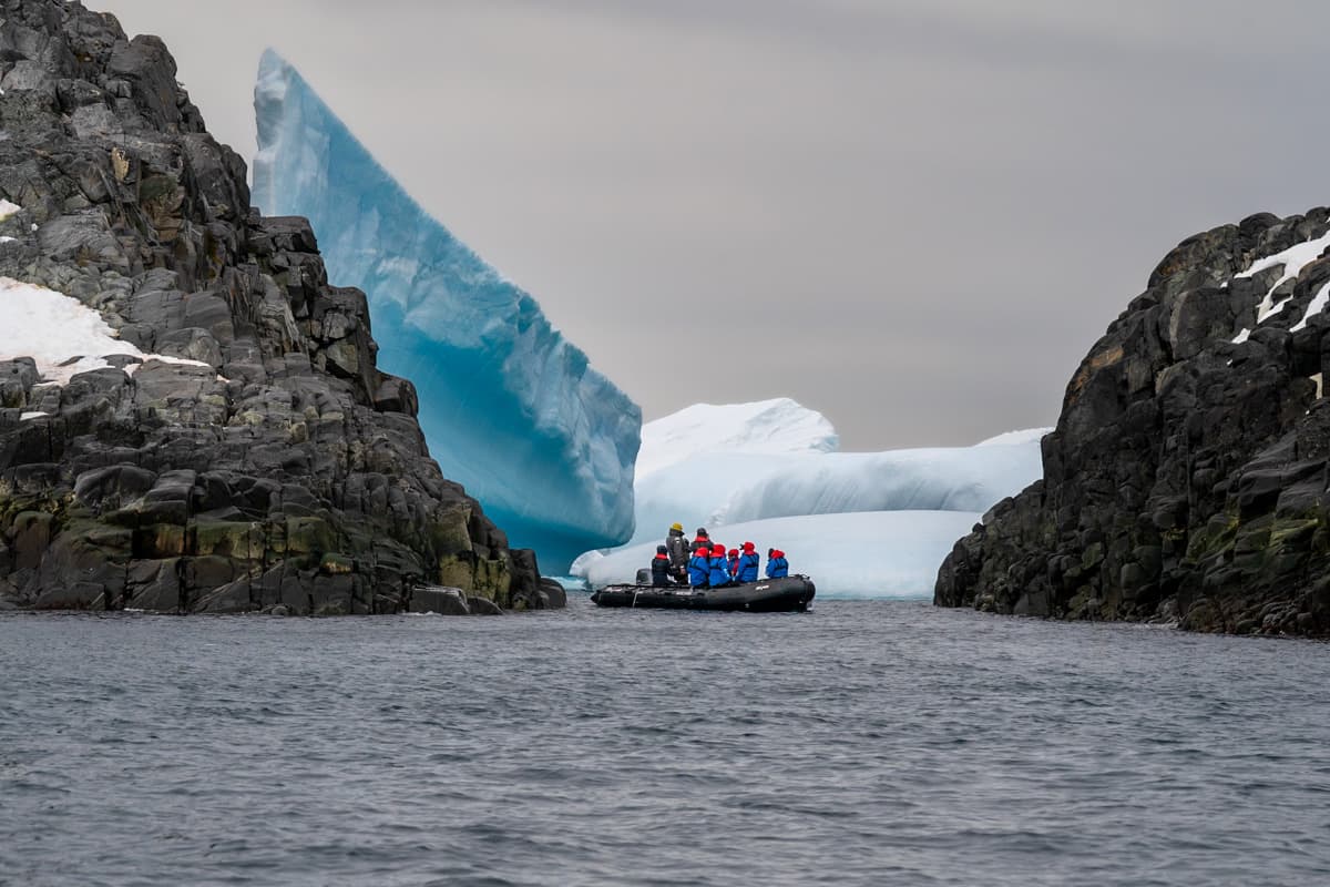 Zodiac boat between two cliffs with icebergs in the background on an Antarctica cruise