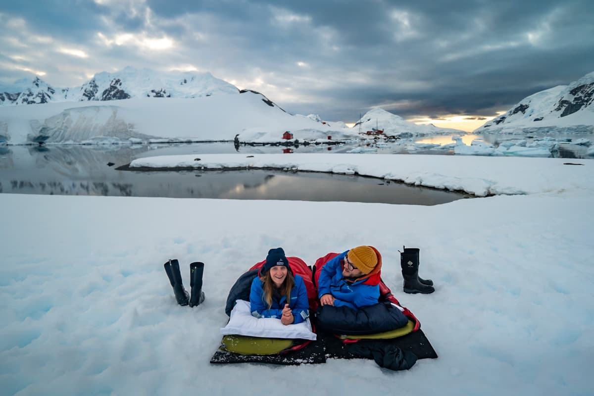 Couple lying on the snow with snow covered mountains in the background in Paradise Bay, Antarctica