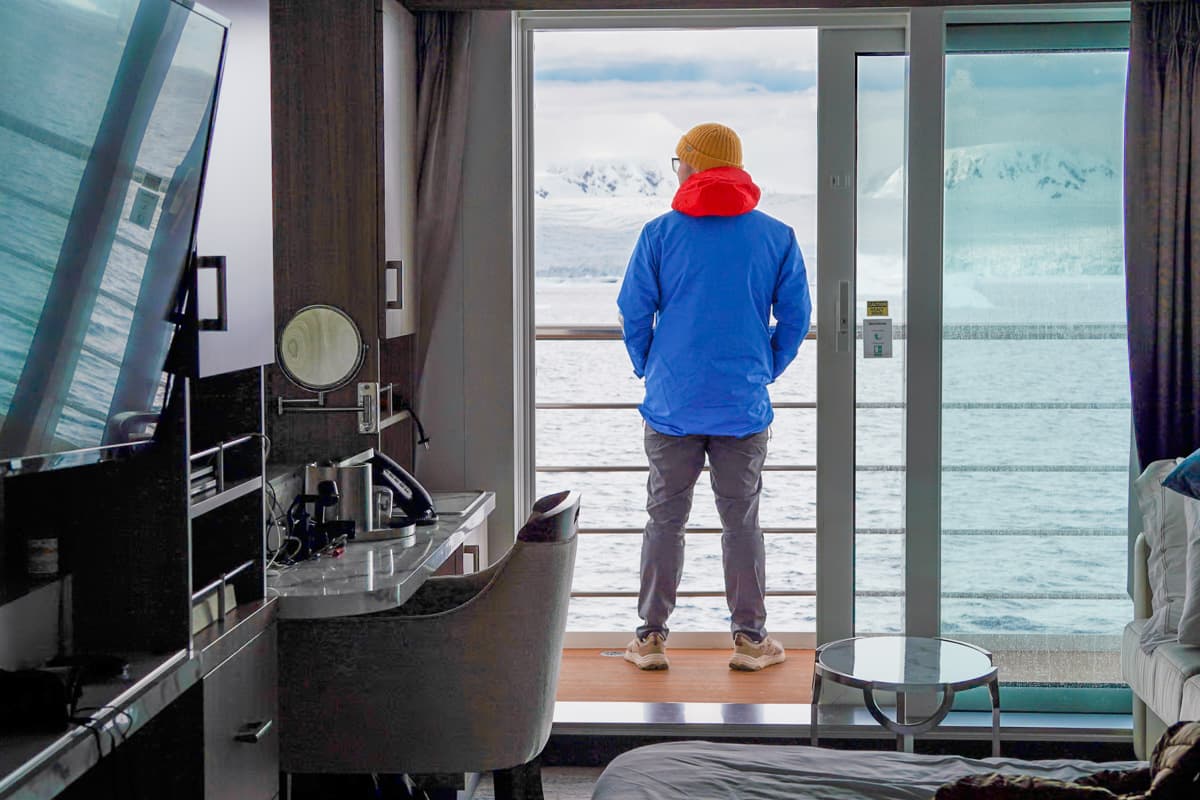 Man standing on the balcony of his cabin with snowy mountains in the background on an Antarctica cruise