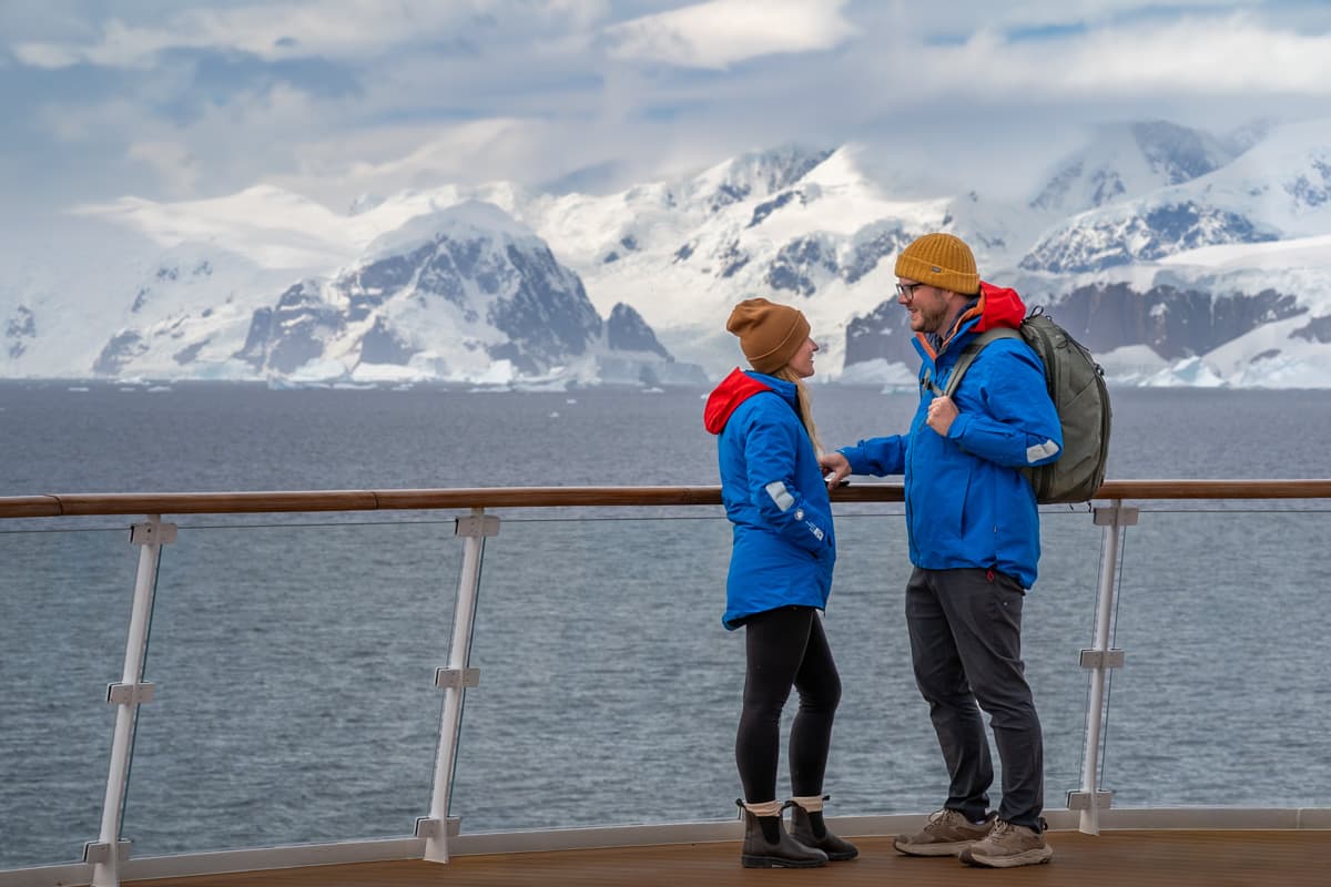 Couple standing on the top deck of an Antarctica cruise with snowy mountains in the background