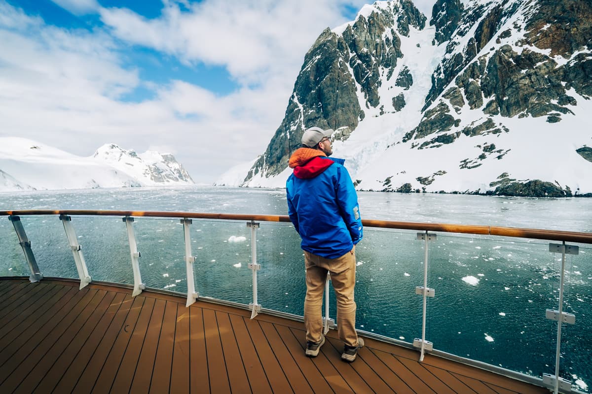 Man standing on a deck with a snowy mountain in the background on the Lemaire Channel on an Antarctica cruise