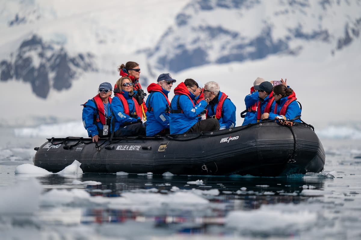 Expedition guide piloting a Zodiac boat through sea ice with a snowy mountain in the background on an Antarctica cruise