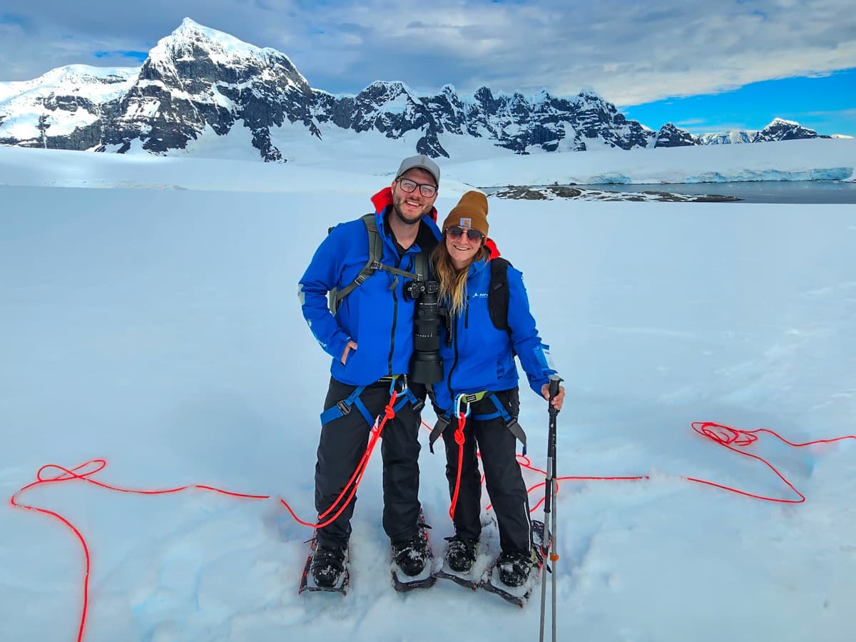 Smiling couple wearing snowshoes with jagged mountains in the background in Antarctica