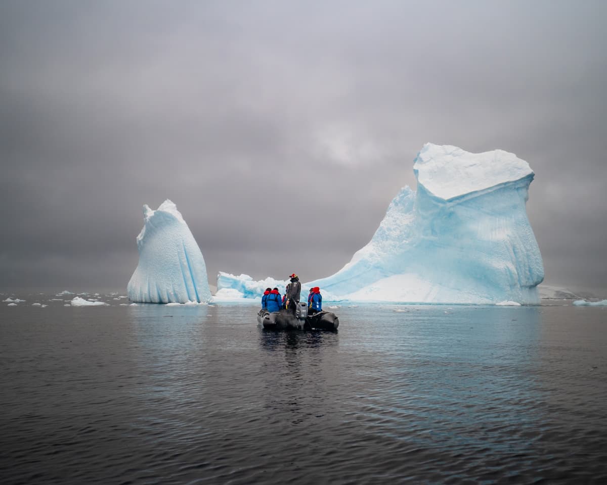 Expedition guide with guests in a Zodiac boat with a large iceberg in the background on an Antarctica cruise
