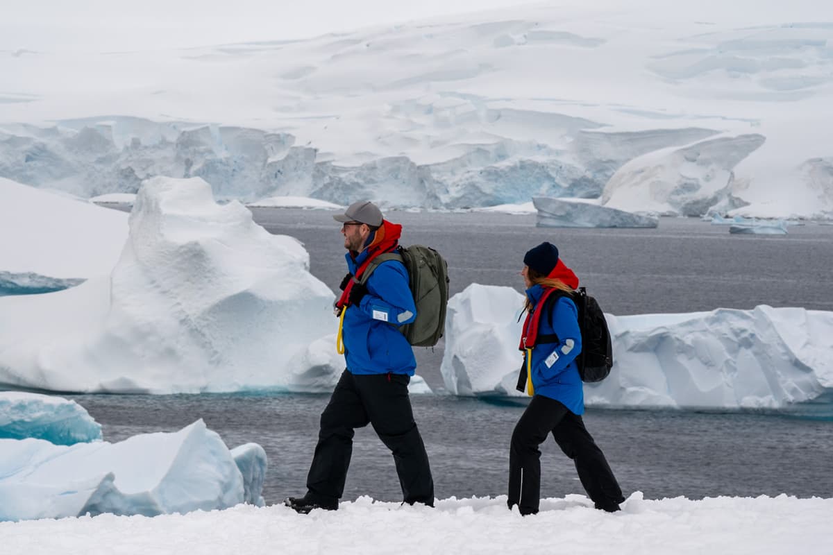 Couple hiking through the snow with icebergs in the background in Antarctica