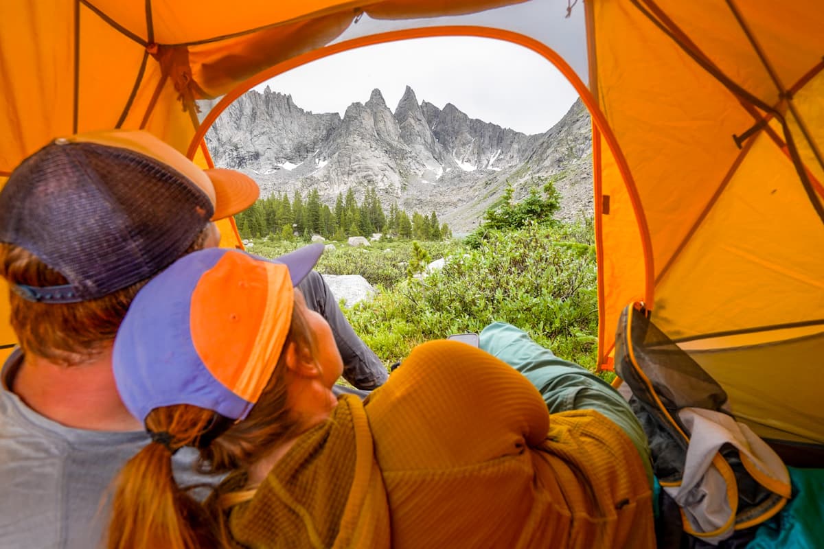 Couple laying in a tent looking at the backside of the Cirque of the Towers near Shadow Lake in the Wind River range of Wyoming