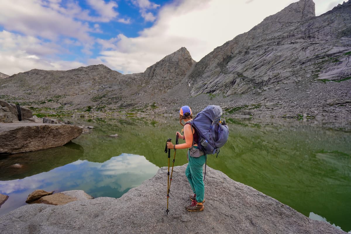 Woman standing on a rocky outcropping with Texas Lake and rugged mountains in the background along the Cirque of the Towers Trail in Wyoming