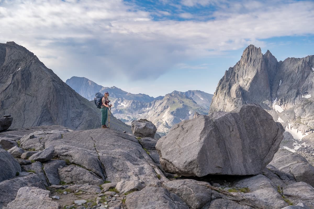 Woman standing on a rocky outcropping with rugged mountains in the background along the Cirque of the Towers Trail in the Wind River range of Wyoming