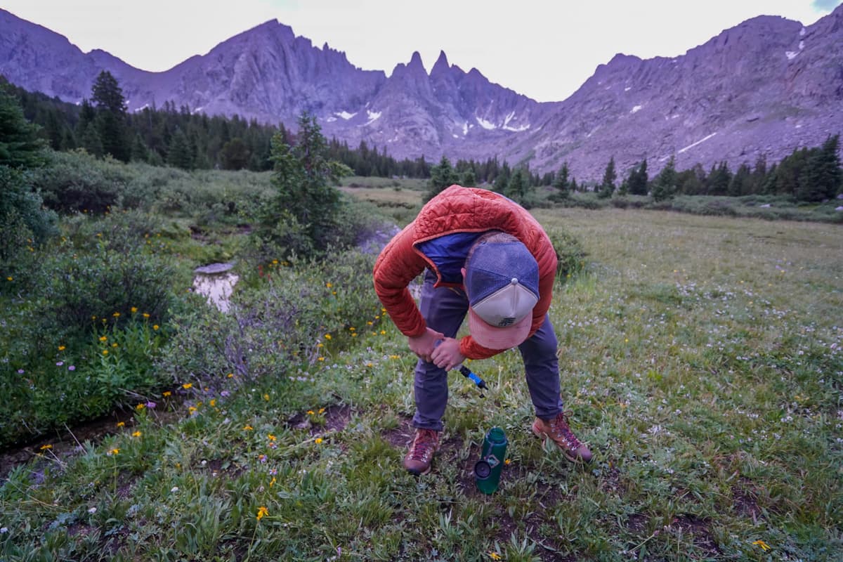 Man filtering water into a water bottle with the Cirque of the Towers in the background in the Wind River range in Wyoming