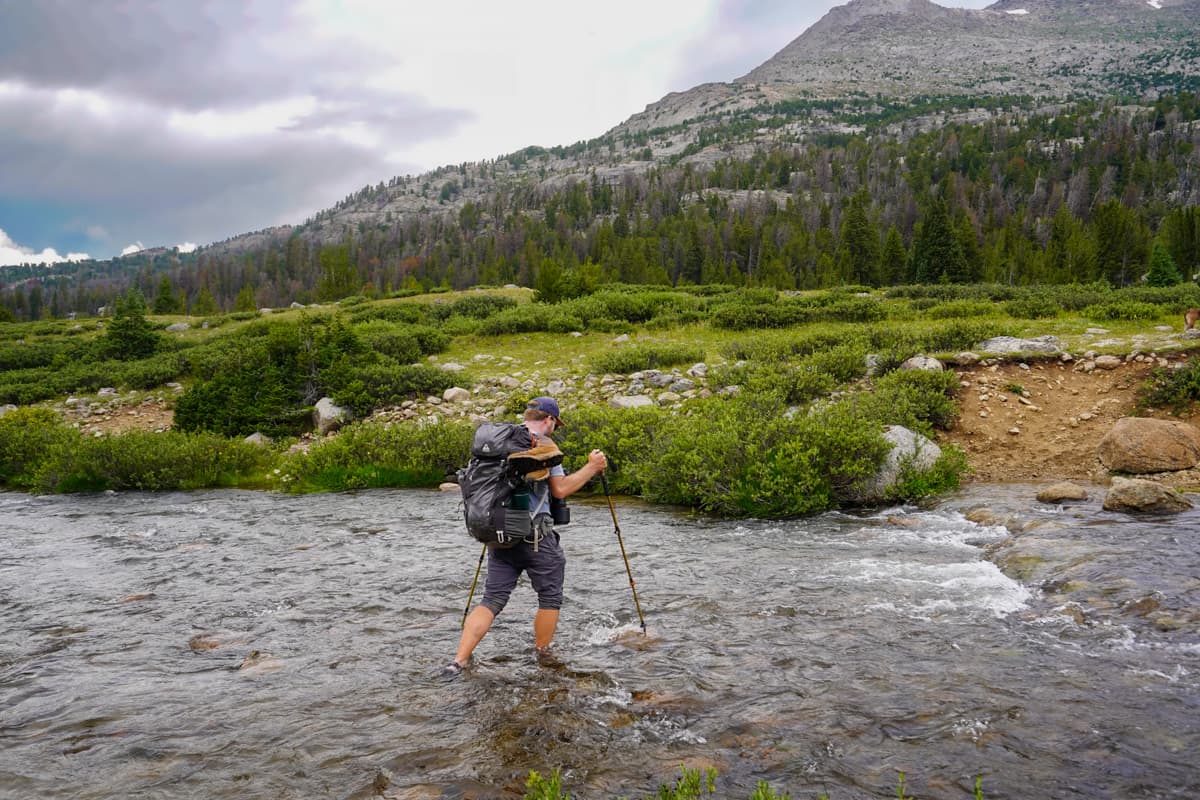 Man walking across the Washakie Creek along the Cirque of the Towers Trail in the Wind River range of Wyoming