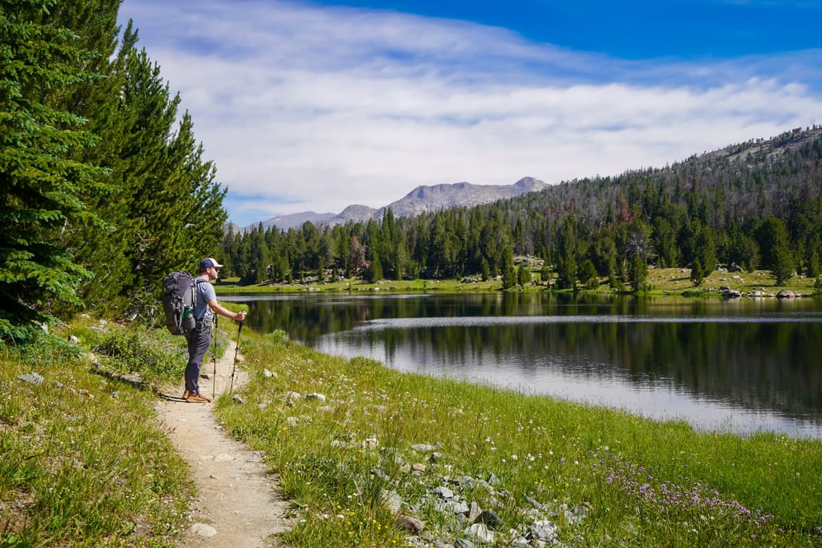 Man with trekking poles standing along hte Cirque of the Towers trail on the shoreline of Mirror Lake in the Wind River range in Wyoming