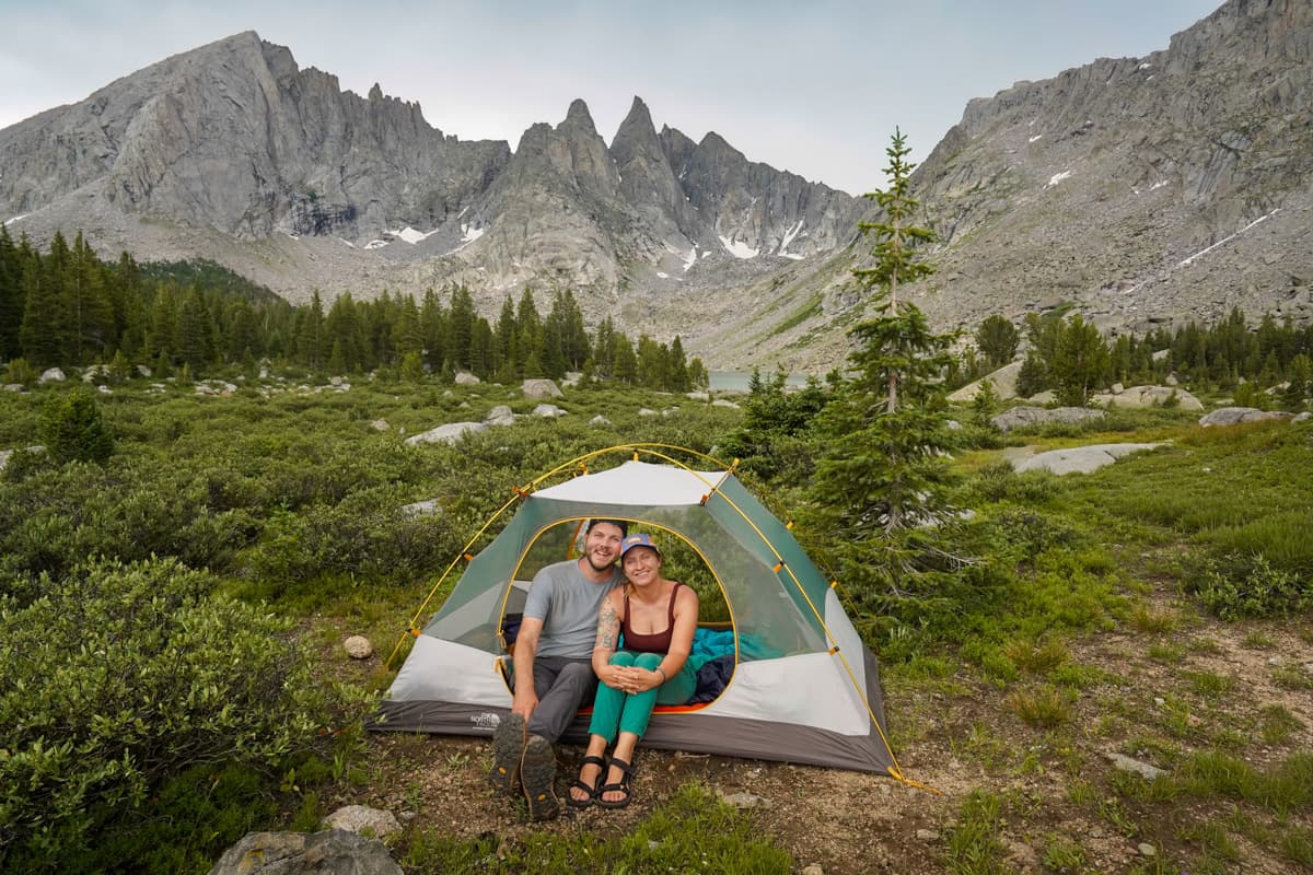 Couple sitting in a tent with Shadow Lake and the backside of the Cirque of the Towers in the background in the Wind River range of Wyoming