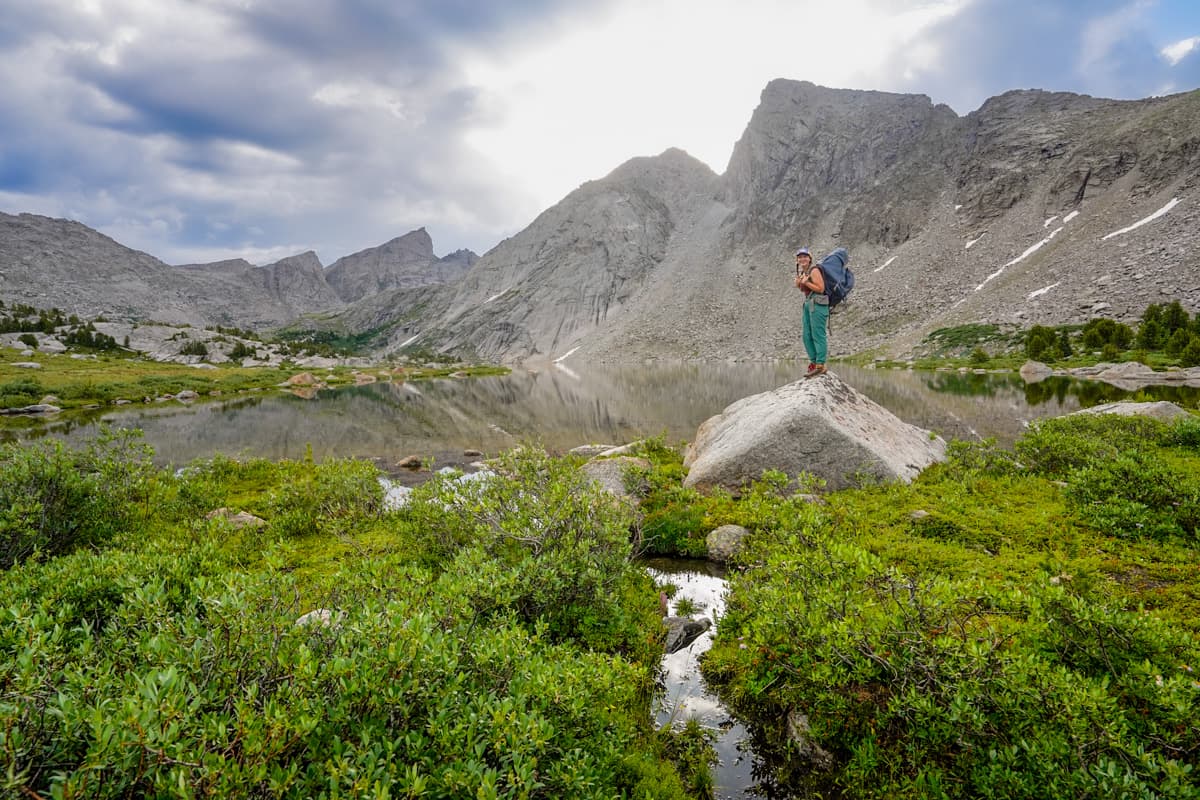 Woman standing on a boulder with Billy's Lake in the background along the Cirque of the Towers trail in the Wind River range of Wyoming