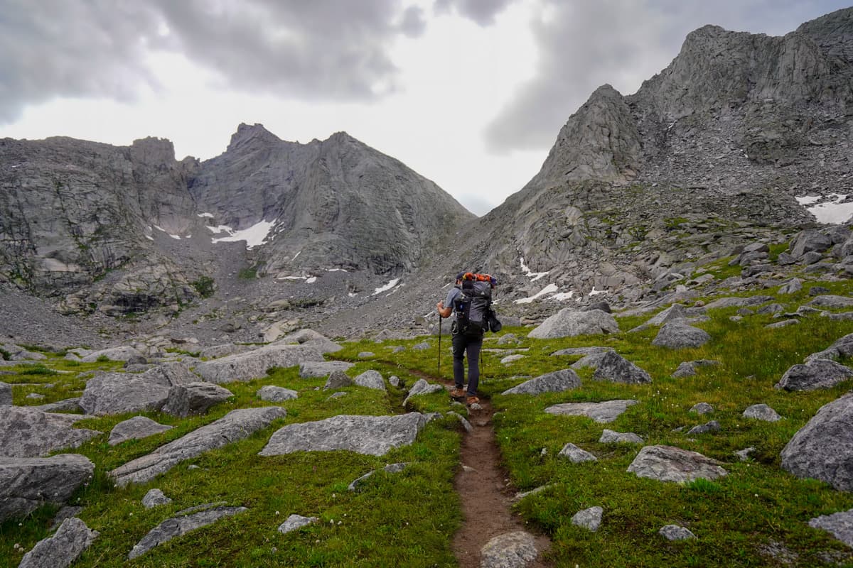 Man walking up a dirt path towards Texas Pass with Cirque of the Towers in the background in the Wind River range in Wyoming